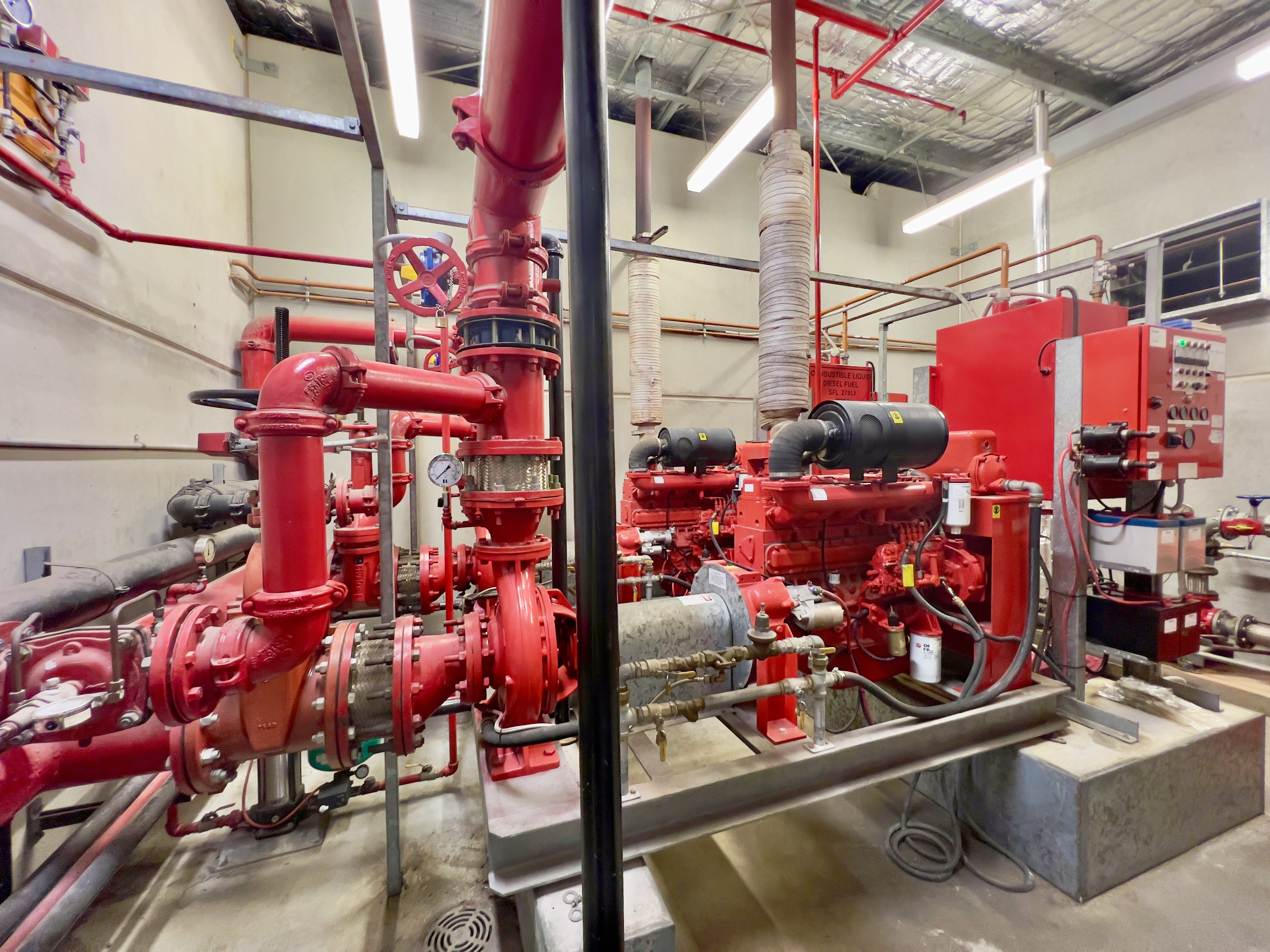 Red diesel fire pumps, red fire-protection piping, and a fire pump controller in a plant room